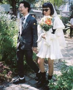 a man and woman dressed in wedding attire walking down a path with flowers on their bouquets