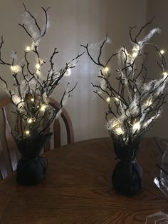 two vases filled with branches and lights on top of a wooden dining room table