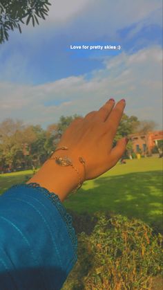 a woman's hand with a ring on it in front of a green field