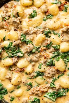 a skillet filled with pasta and spinach covered in gravy on top of a wooden table