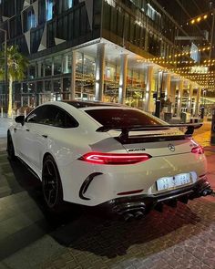 a white sports car parked in front of a tall building at night with its lights on