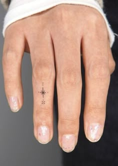 a woman's hand with a small compass tattoo on her left thumb and finger