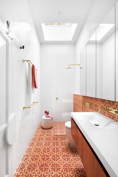 a bathroom with an orange and white tile floor, skylight above the toilet and sink