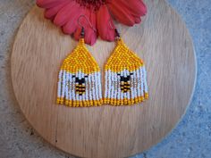 two yellow and white beaded earrings sitting on top of a wooden table next to a flower