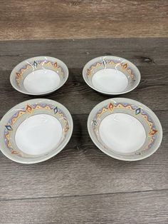 four plates with designs on them sitting on a wooden floor next to a bowl and spoon