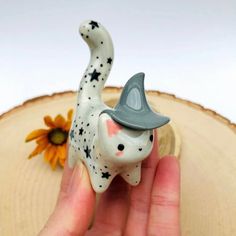 a hand holding a small ceramic cat figurine with a hat on it's head