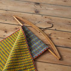 a knitted triangle next to a knitting needle on a wooden floor with a measuring tape