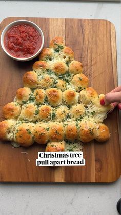 a christmas tree made out of rolls on top of a cutting board next to a bowl of sauce