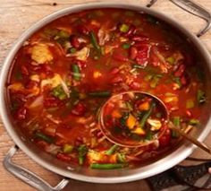 a pot filled with soup and vegetables on top of a wooden table next to utensils