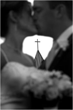 a bride and groom kissing in front of a cross