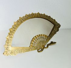 an antique brass fan shaped mirror on a white surface