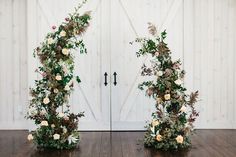 two white doors with flowers and greenery on them in front of a wooden floor