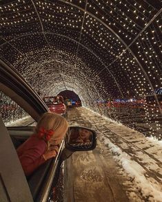 a woman driving down a snow covered road in front of a tunnel filled with christmas lights