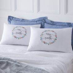 two pillows with embroidered sayings on them sitting on a bed in front of a white headboard