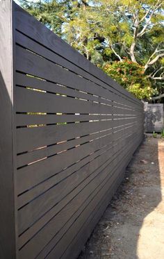 the side of a black fence with wooden slats on it and trees in the background