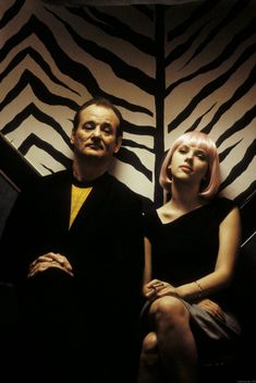 a man and woman sitting next to each other in front of a zebra print wall