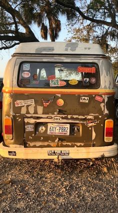 an old van with stickers on it parked in the dirt next to some trees