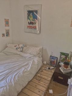 a bed with white sheets and pillows on top of a wooden floor next to a table