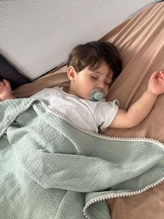 a little boy laying in bed with a pacifier on his mouth and sleeping under a blanket