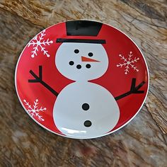 a red and white plate with a snowman painted on the side, sitting on a marble surface