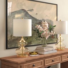 a table with two lamps and a painting on the wall above it that has flowers in a vase