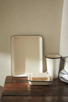 a square plate, soap dish and cup sit on a wooden table in front of a white wall