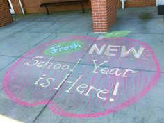 chalk writing on the sidewalk that says new school year is here and an apple with leaves