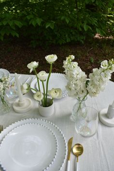 the table is set with white flowers in vases and silverware, along with other dishes