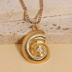 a gold necklace with a pearl in the center on a beige surface, next to a white brick wall