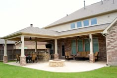 a patio with an outdoor fireplace and grill area in the middle of it, surrounded by grass