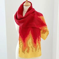 a red and yellow knitted scarf sitting on top of a white mannequin