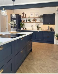 a kitchen with blue cabinets and white counter tops, an island in the middle is surrounded by potted plants