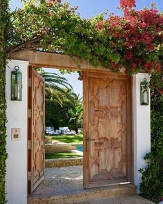 two wooden doors are open in front of a white building with flowers growing on it