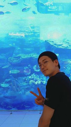 a man standing in front of a large fish tank with his finger up to the camera