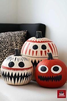 three painted pumpkins sitting next to each other on a white couch with black and red pillows