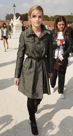 a woman in a trench coat and black pants is walking down the street with another woman behind her