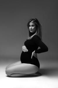 a pregnant woman sitting on the floor posing for a black and white photo with her hands behind her back