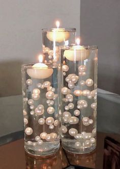 two glass vases filled with pearls and lit candles