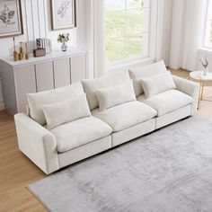 a living room with white couches and rugs on the hardwood floor, along with two windows