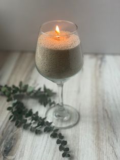 a candle that is sitting in a wine glass with some leaves on the table next to it