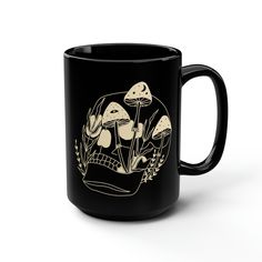 a black coffee mug with an image of mushrooms in the forest on it's side