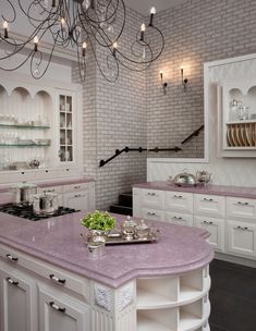 a large kitchen with white cabinets and pink counter tops, chandelier hanging from the ceiling