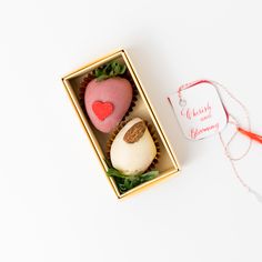 two heart shaped chocolates in a box on a white surface with a red string