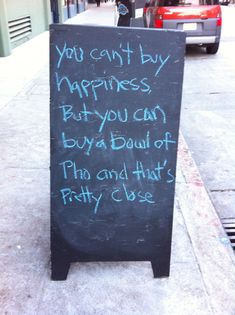 a sign on the sidewalk that says, you can't buy happiness but you can buy a dad of pizza and hot dogs