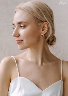 a woman with blonde hair wearing earrings and a white dress looking off to the side