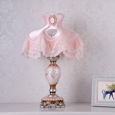 a pink lamp sitting on top of a white table next to a framed photo and an animal