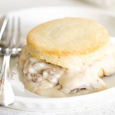 a white plate topped with a biscuit covered in gravy next to a fork