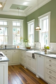 a kitchen with green walls and white cabinets, wood flooring and an island in the middle