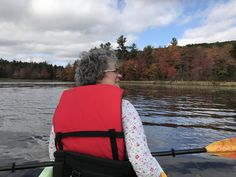 an older woman in a red life jacket paddling a kayak on a lake