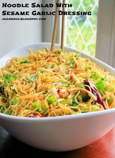 noodle salad with sesame garlic dressing in a white bowl on a wooden table next to a window